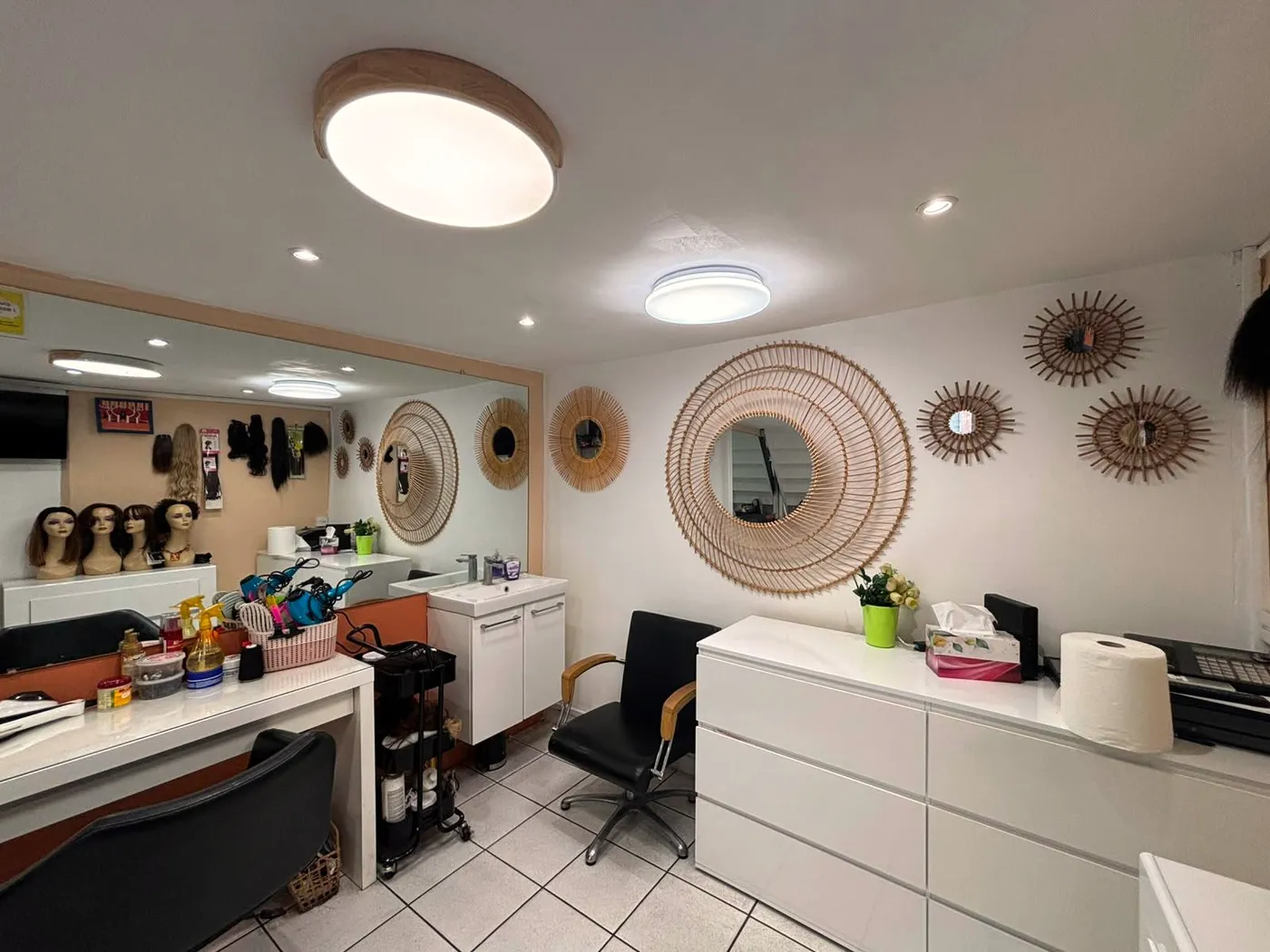 L'intérieur du salon Cosmetex : miroirs en rotin, têtes à perruques et fauteuils